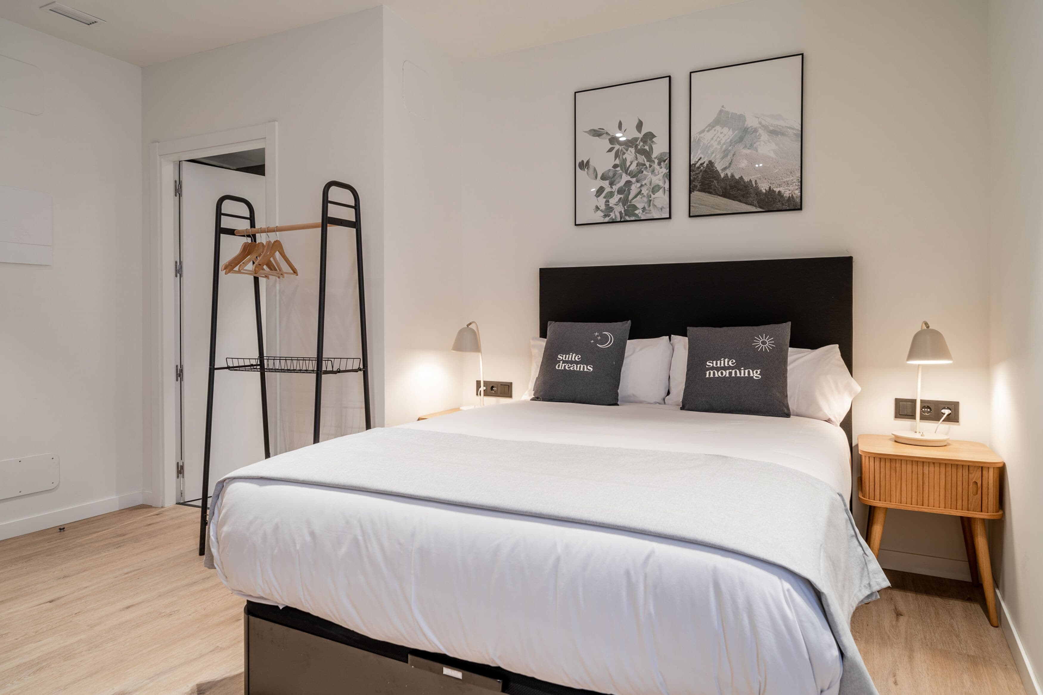 A neatly made bed with a black headboard, two bedside tables with lamps, and a door with a coat rack.