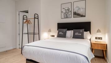 A neatly made bed with a black headboard, two bedside tables with lamps, and a door with a coat rack.