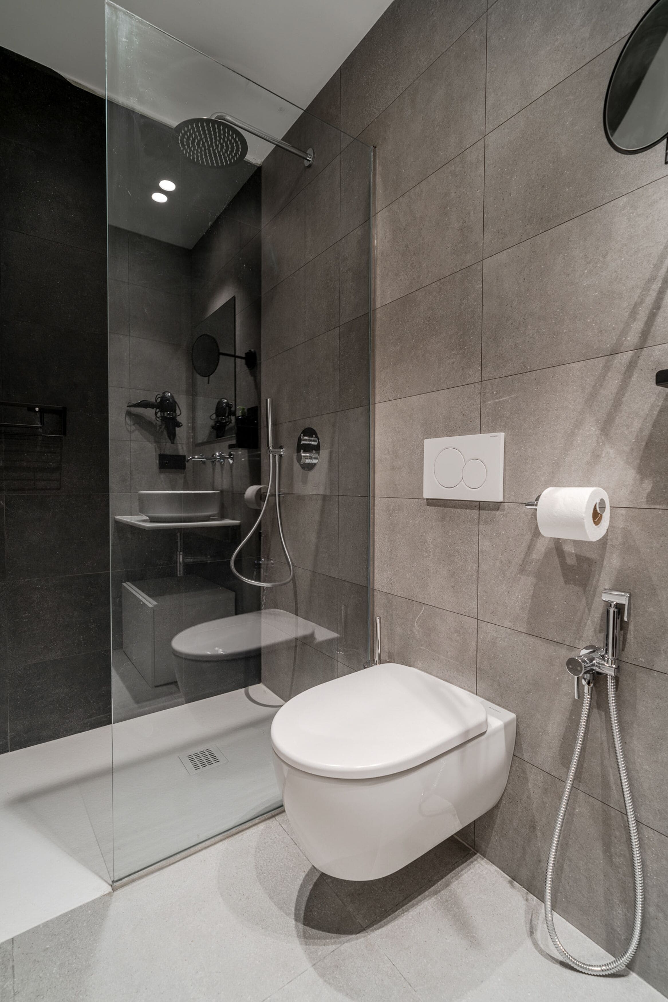 A modern bathroom with a glass-enclosed shower, a white toilet, and a wall-mounted toilet paper dispenser.