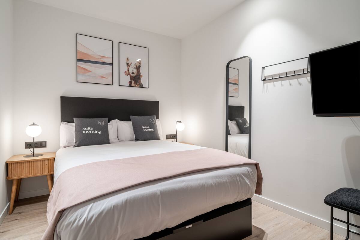 A modern bedroom with a large bed, bedside tables with lamps, a bench, and artwork on the wall.