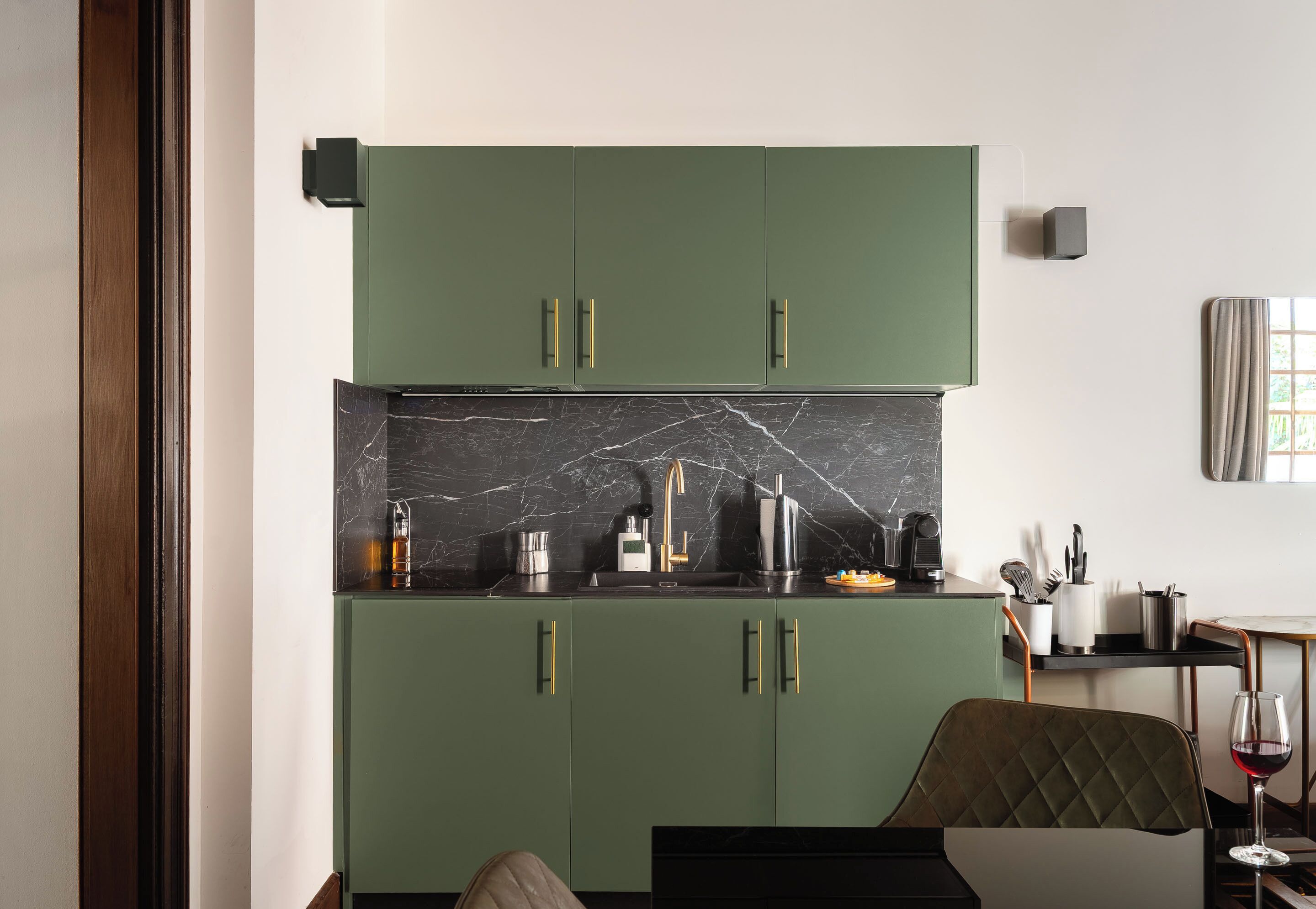 Cozinha moderna com armários verdes, painel de backsplash em mármore e área de refeições com uma cadeira e mesa.