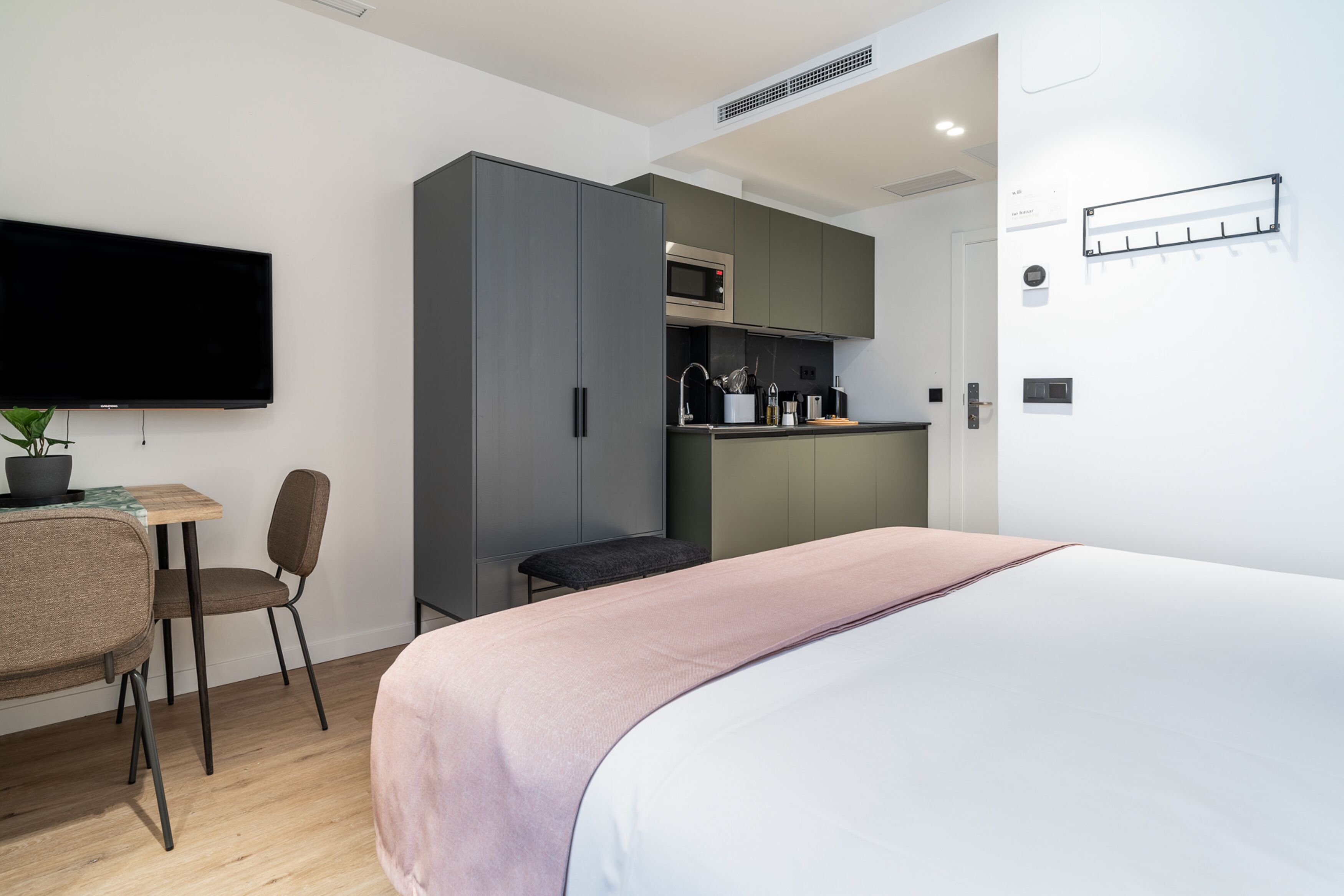 Une chambre d’hôtel moderne équipée d’un lit, d’un bureau, d’une chaise, d’une kitchenette et d’un téléviseur à écran plat.