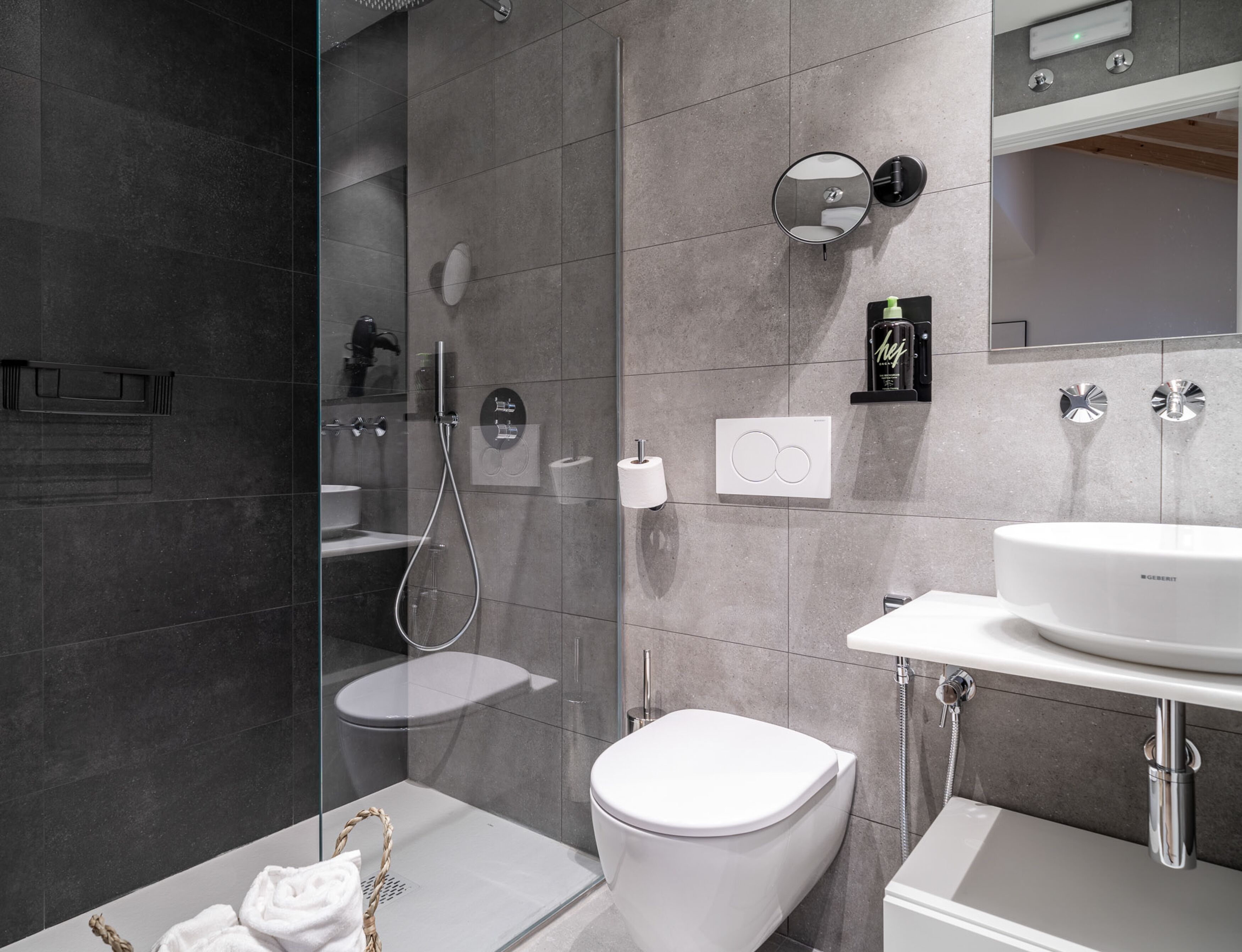 A modern bathroom with a glass-enclosed shower, a toilet, a sink, and a mirror.