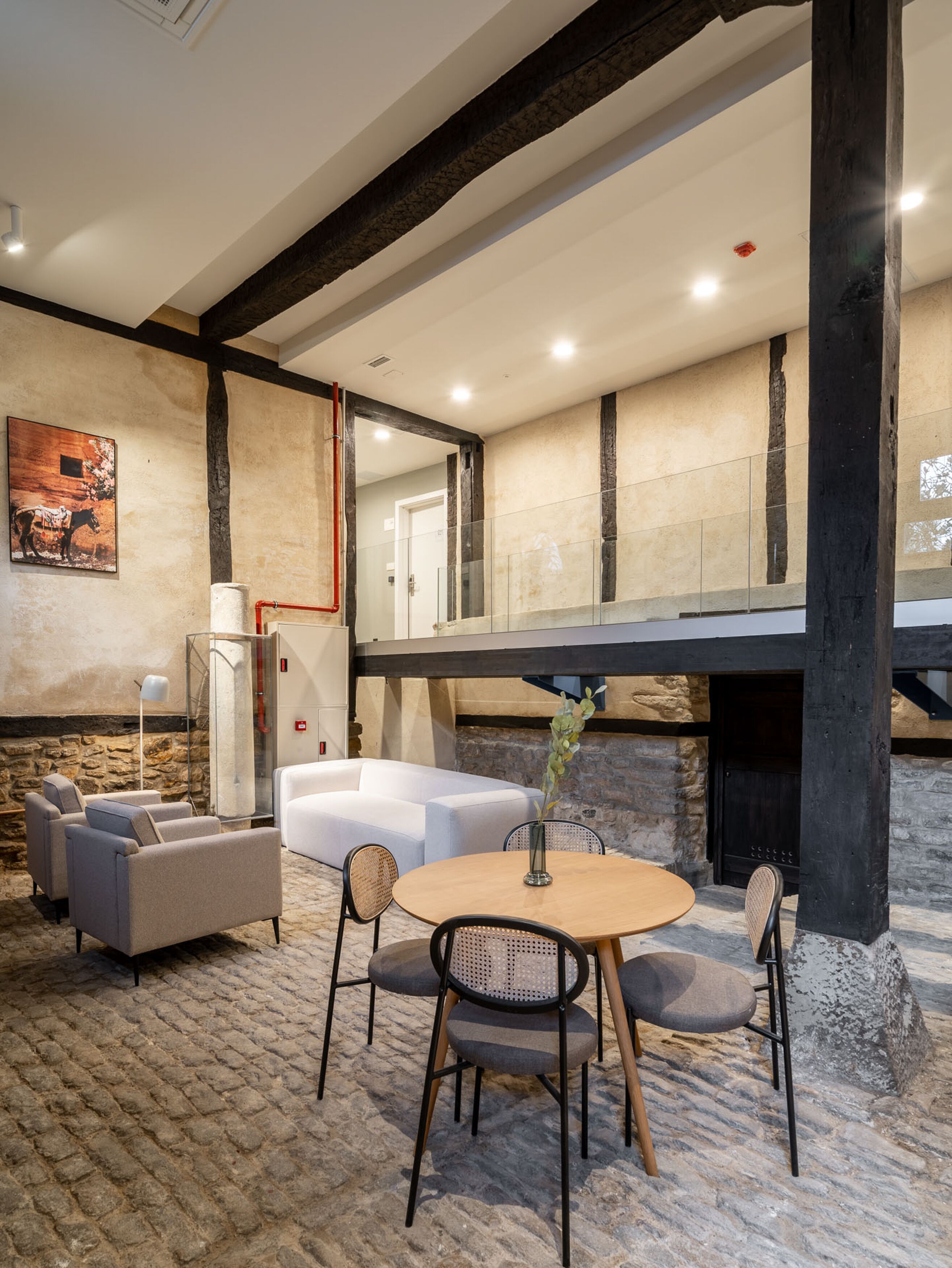 Un interior moderno con suelo de piedra, una mesa redonda de madera con sillas, un sofá blanco y una chimenea.