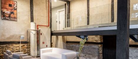 Un interior moderno con suelo de piedra, una mesa redonda de madera con sillas, un sofá blanco y una chimenea.