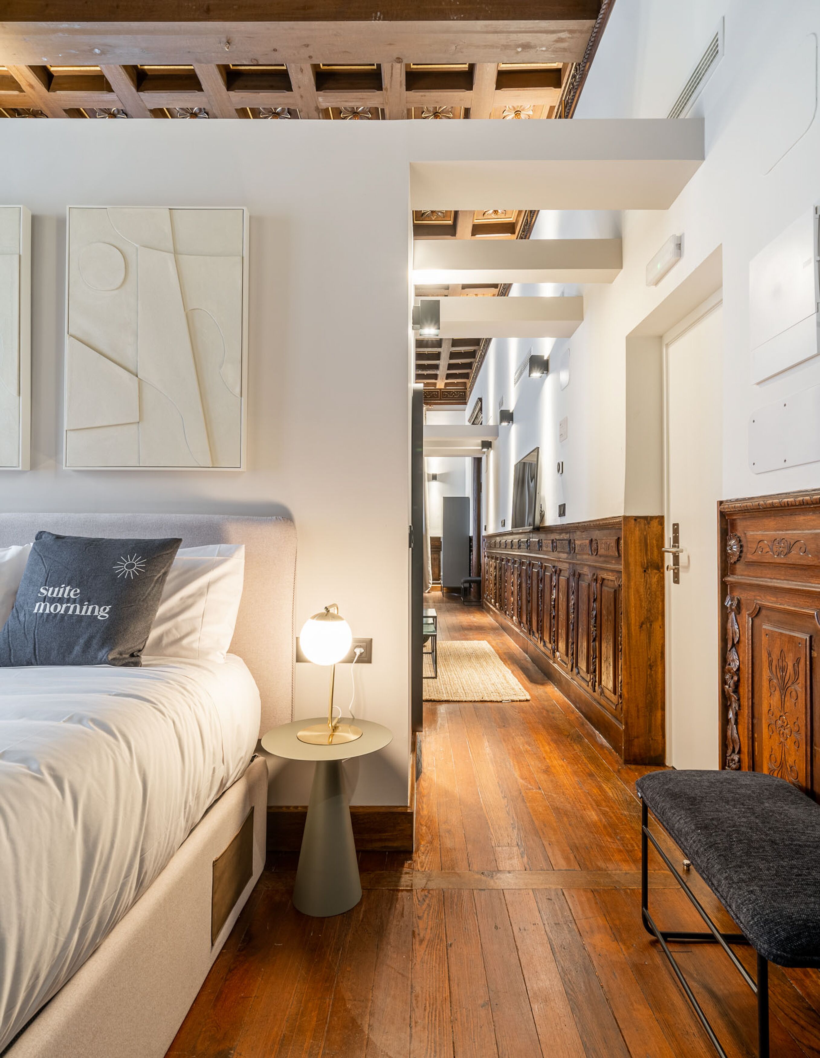 Una habitación de hotel con cama, mesita de noche, lámpara y un banco.