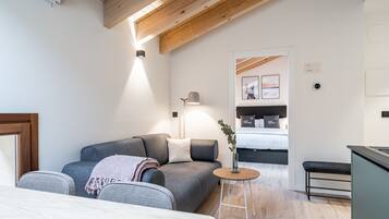A modern bedroom with a grey sofa, a small round table, a bed, and a desk area.