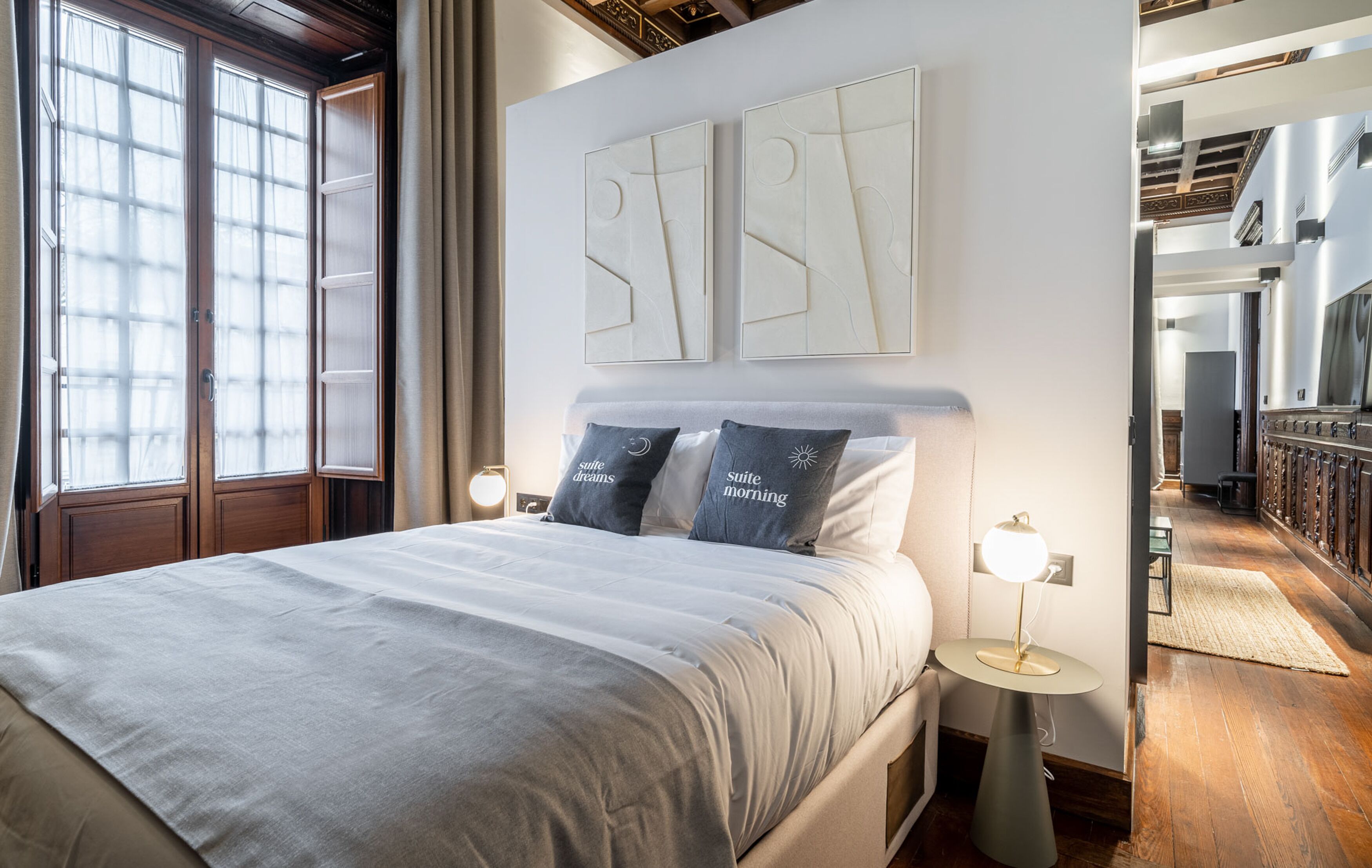 Un dormitorio ordenado con una cama grande, dos lámparas de noche y vistas a una escalera de madera.