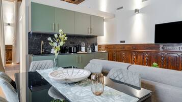 A modern kitchen with green cabinets, a marble countertop, and a dining area with a glass table and grey upholstered sofa.