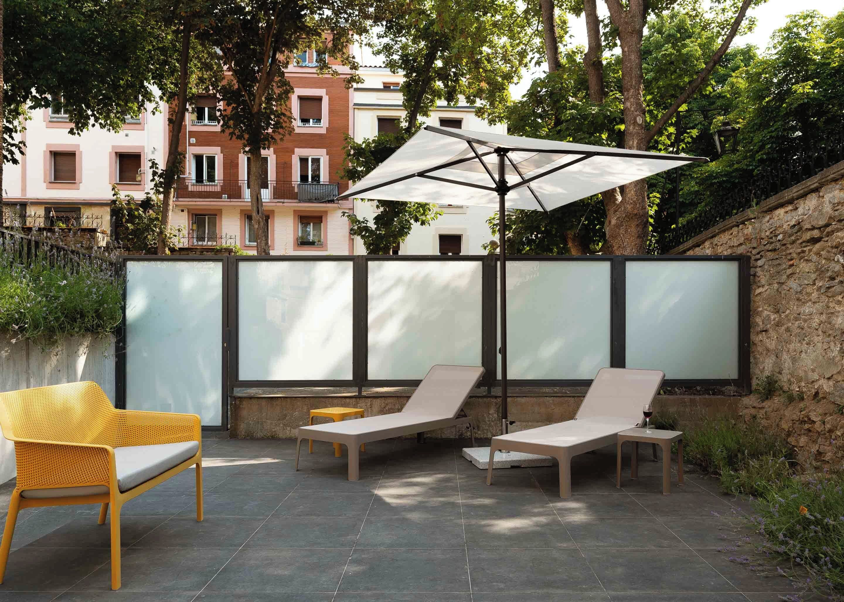 A patio with two lounge chairs, a yellow wicker chair, and a large umbrella.