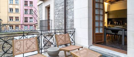 A balcony with wicker furniture, a stone wall, and a view of colorful buildings.