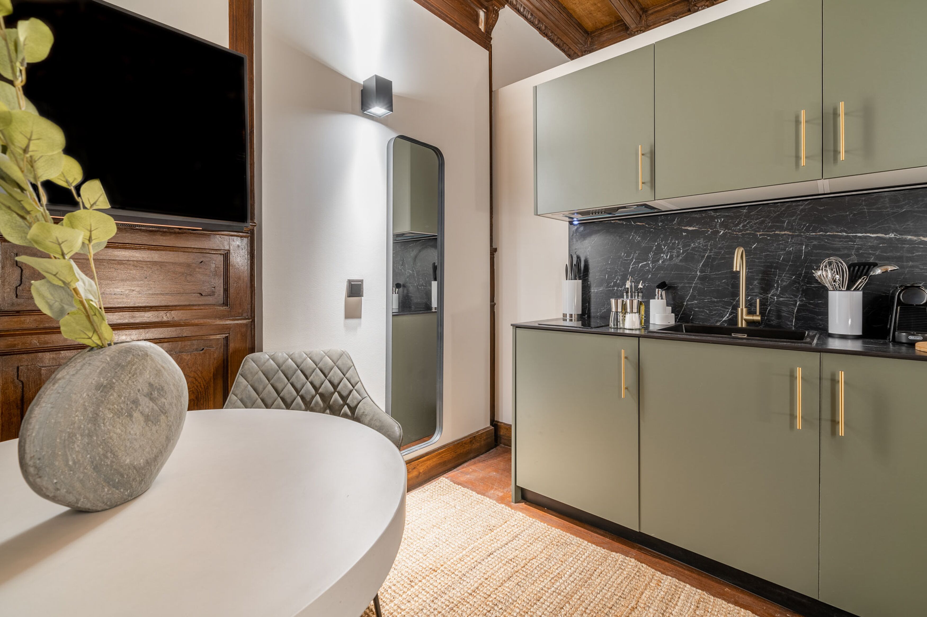 A modern kitchen with green cabinets, a marble backsplash, and a stone centerpiece on the table.