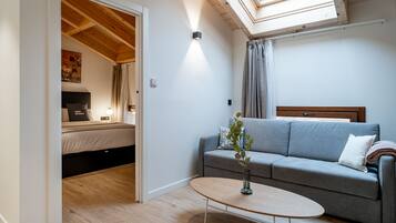 Ein modernes Schlafzimmer mit Dachfenster, einem grauen Sofa und einem Nachttisch.