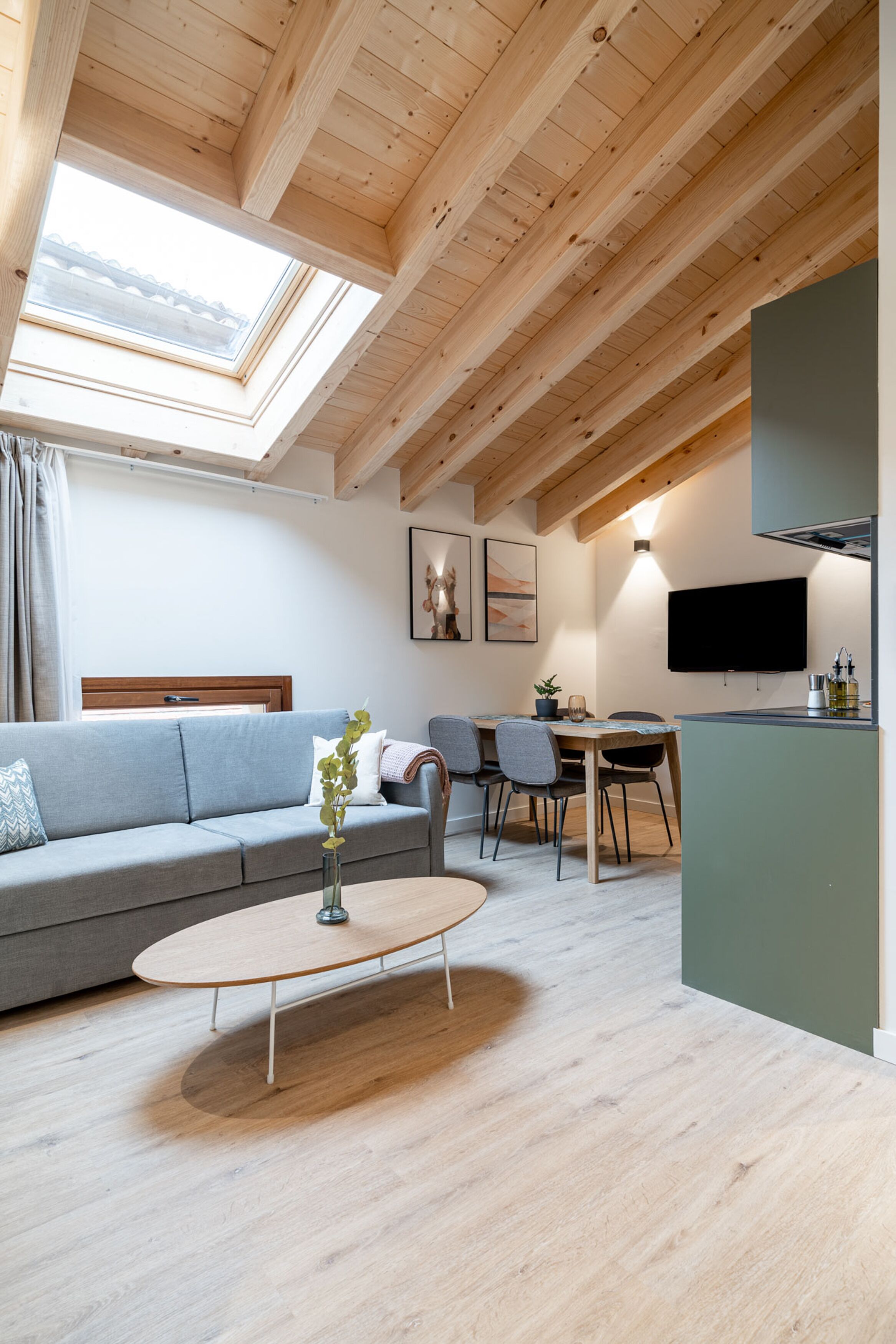 Una sala moderna con sofá, mesa de comedor y sillas, televisor montado en la pared y tragaluz.