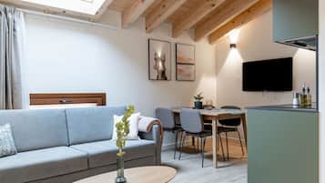 Una sala moderna con sofá, mesa de comedor y sillas, televisor montado en la pared y tragaluz.