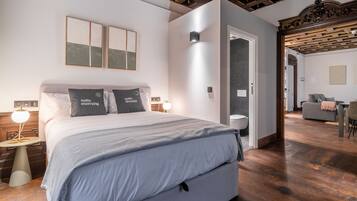 Un dormitorio moderno con una cama grande, mesitas de noche y una mesita auxiliar. Hay una puerta que conduce a otra habitación.