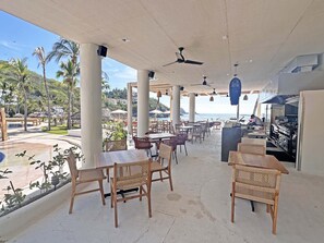 An outdoor cafe with tables and chairs, a view of the sea, and a kitchen area. - Beachfront condo with ocean view, private pool & resort amenities (Bahías de Huatulco)