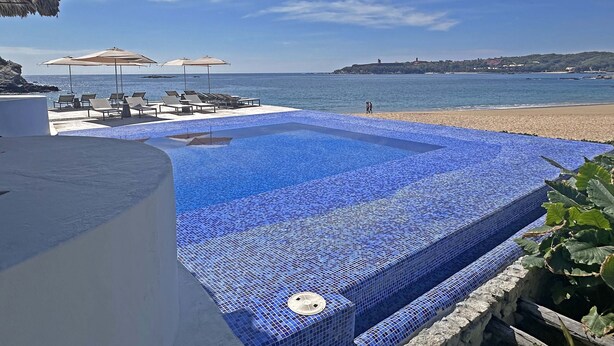 A pool with blue mosaic tiles, lounge chairs, and umbrellas by the beach. - Beachfront condo with ocean view, private pool & resort amenities (Bahías de Huatulco)