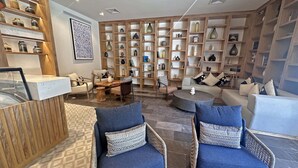 A spacious living area with a wooden bookshelf, a coffee table, and two blue armchairs. - Beachfront condo with ocean view, private pool & resort amenities (Bahías de Huatulco)
