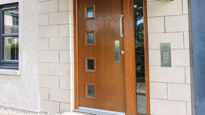 Une porte en bois avec une poignée et un judas, une fente pour le courrier et un luminaire fixé au mur.