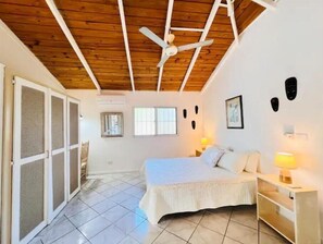 Une chambre à coucher avec un lit, un ventilateur de plafond, une fenêtre et une porte munie d’une moustiquaire.