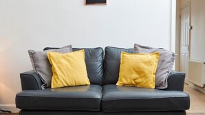 Un divano in pelle nera con due cuscini gialli e due cuscini grigi.