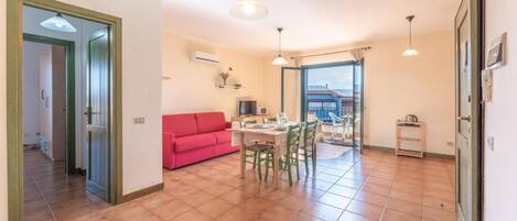 A spacious living area with a red sofa, dining table, and chairs, a kitchen area, and a view through an open door.