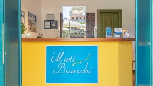 A reception desk with a sign reading "Miti Bianchi" and various informational posters and keychains.