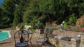 An outdoor patio with a pool, two metal chairs, a small table, and a stone bench with cushions. - Cammino Santo - studio w/private pool & garden (Poggibonsi)