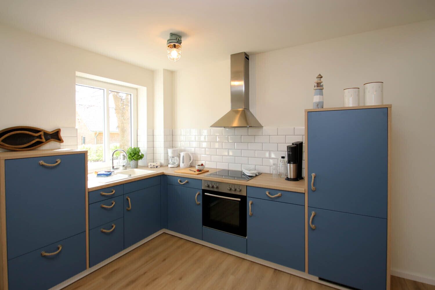 Een kleine keuken met blauwe kastjes, een roestvrijstalen afzuigkap en een raam voor natuurlijk licht.