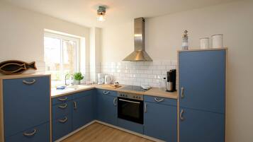 Een kleine keuken met blauwe kastjes, een roestvrijstalen afzuigkap en een raam voor natuurlijk licht.