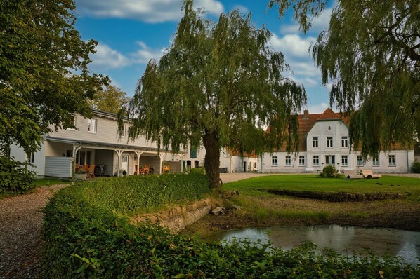 Ein großes, weißes Gebäude mit einer symmetrischen Fassade, einer überdachten Veranda und einem kleinen Teich im Vordergrund.