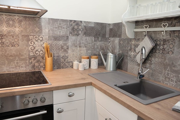 A kitchen with a modern design, featuring a stainless steel sink, wooden countertop, and patterned backsplash.