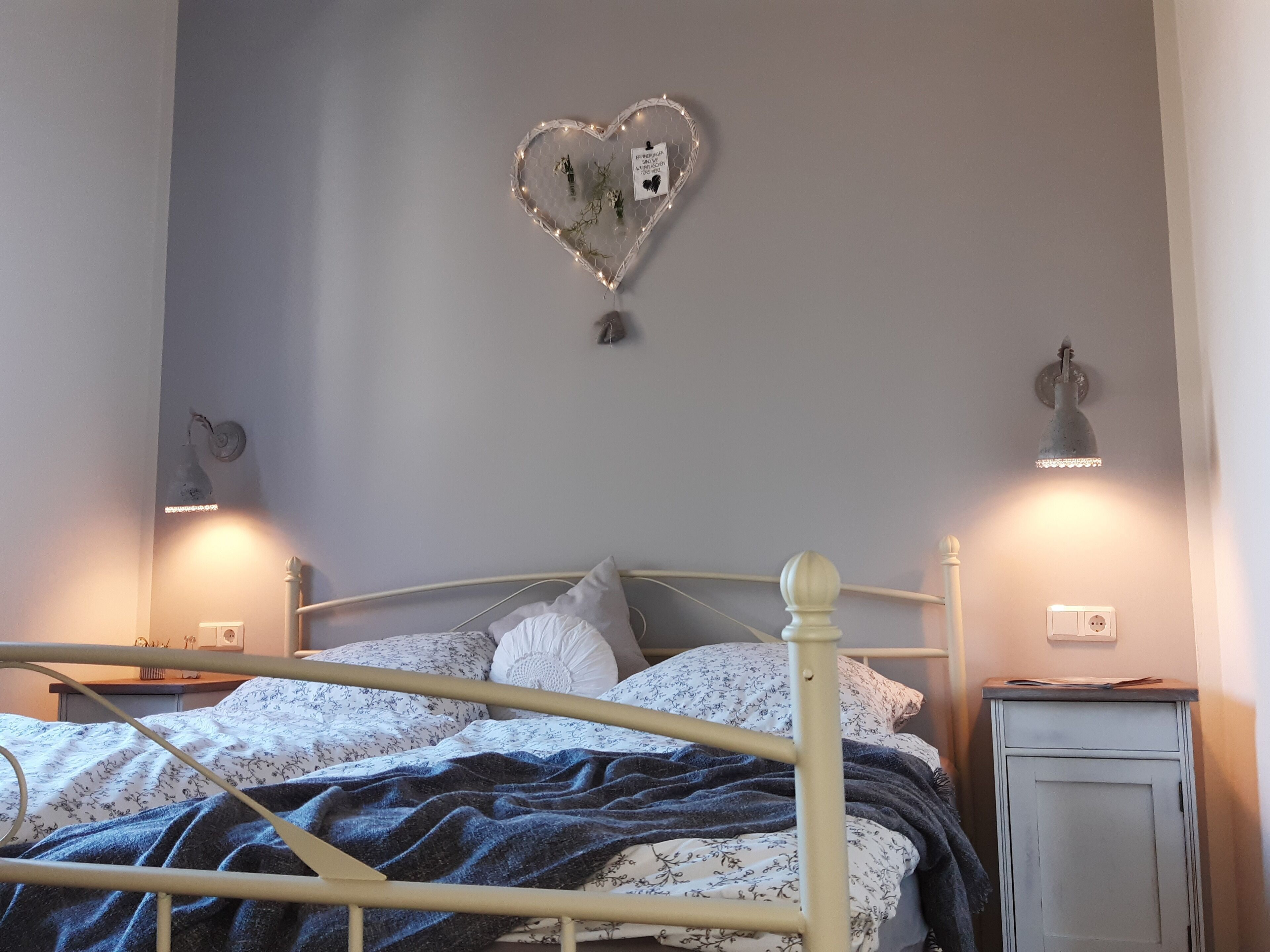 Un dormitorio con cama, un adorno en forma de corazón y dos lámparas de pared.