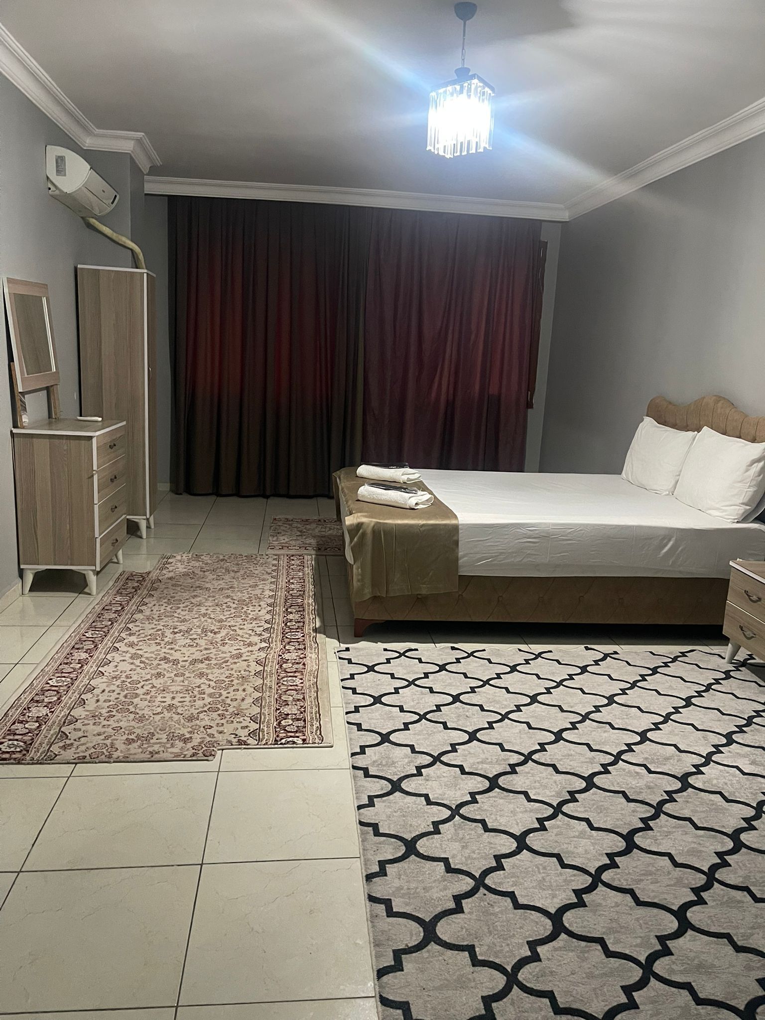 Una camera da letto con un letto, una cassettiera, uno specchio, un lampadario e un tappeto decorato.