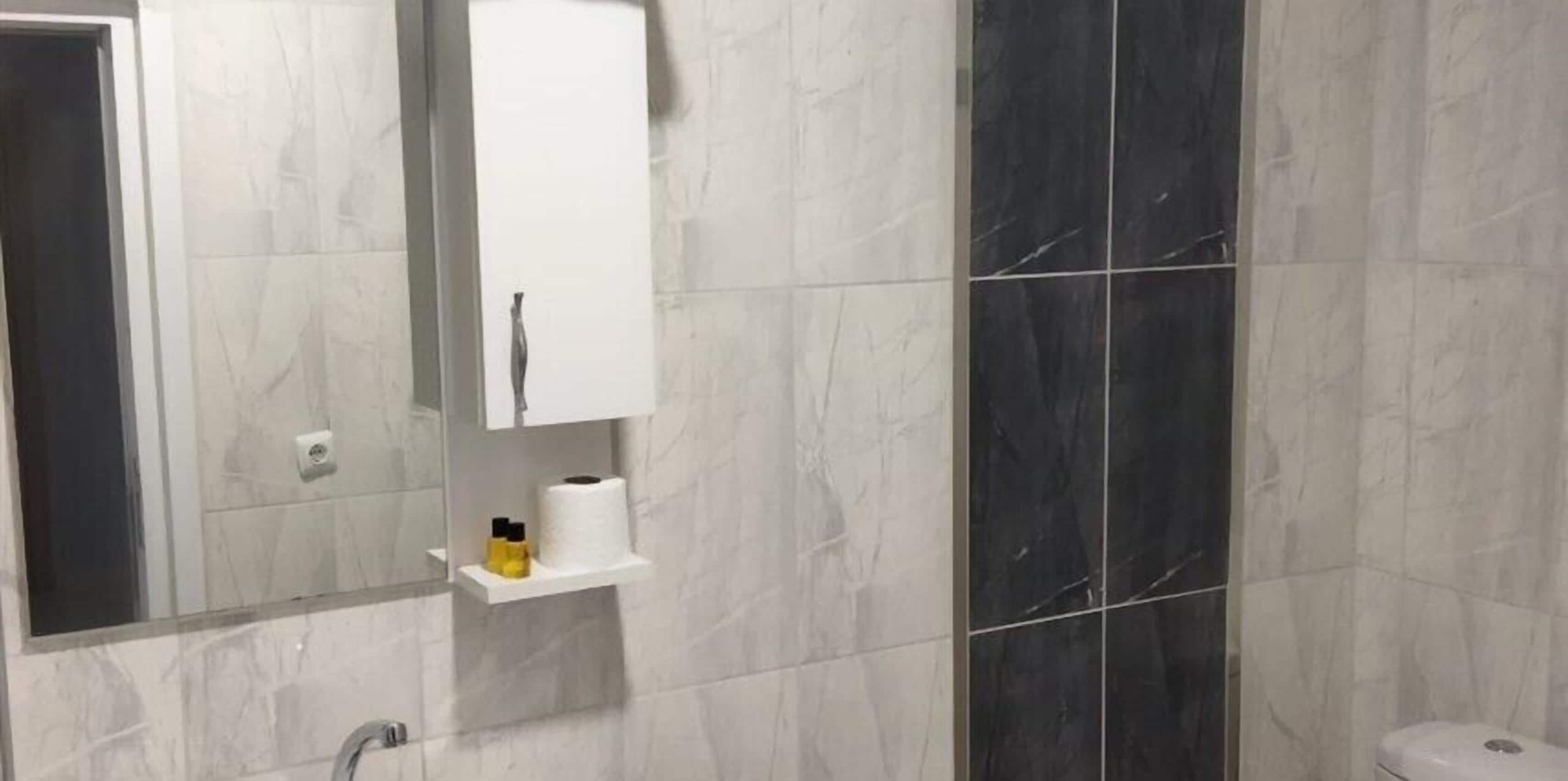 Et badeværelse med marmort gulvfliser, et hvidt skab og en hylde med toiletartikler.