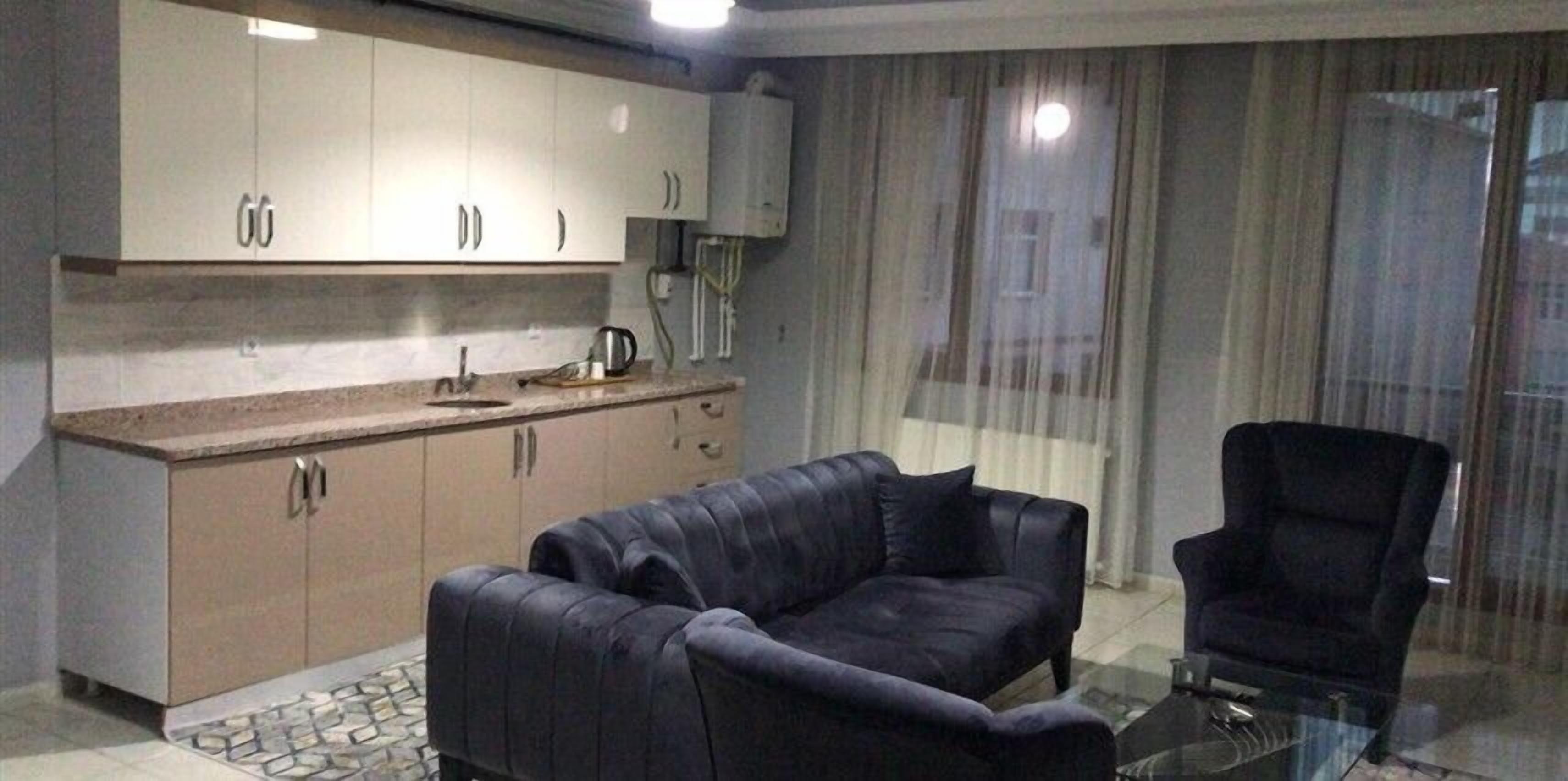 A modern kitchen with a sofa and armchair, a coffee maker, and a window with curtains.