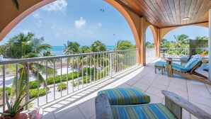 Un balcon avec vue sur l’océan, des palmiers et des chaises longues.