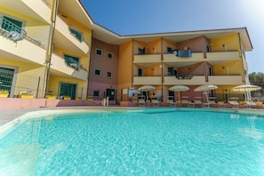 En swimmingpool med en bygning, der har flere balkoner, og en klar blå himmel.