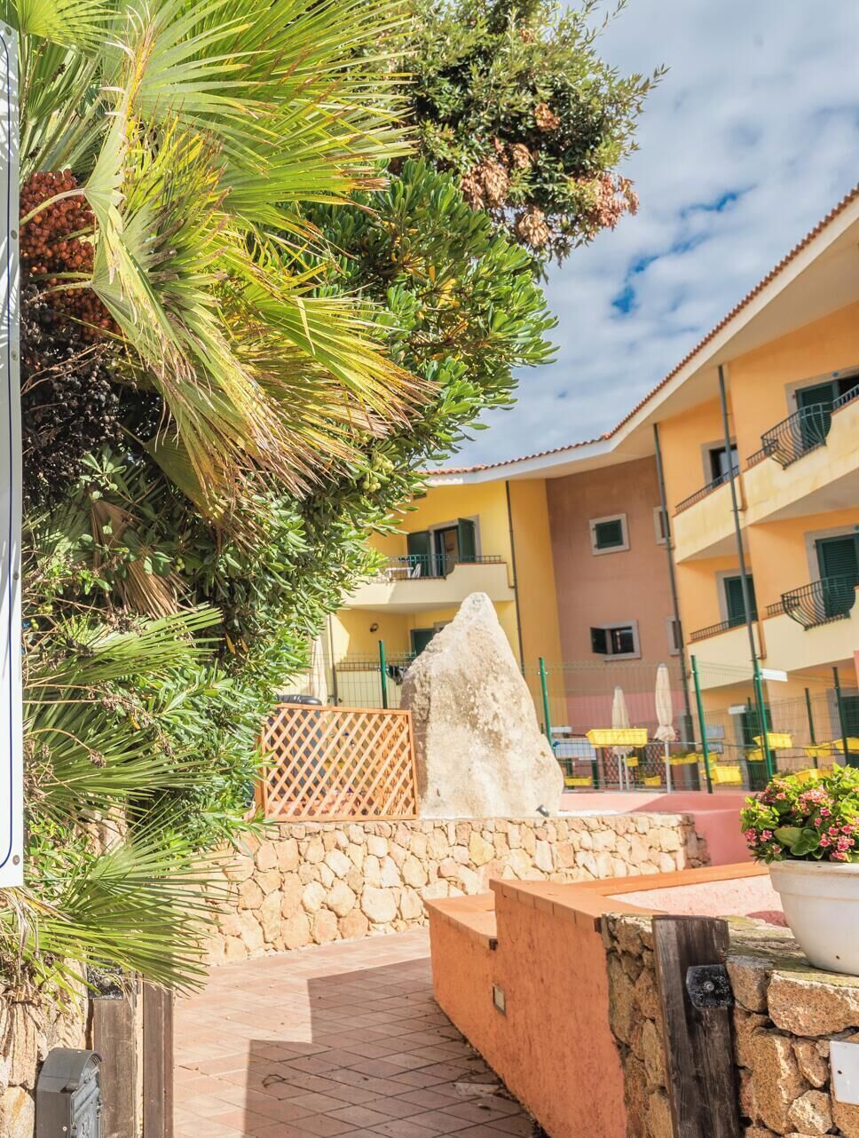 A courtyard with a stone wall, a large rock, and a palm tree.