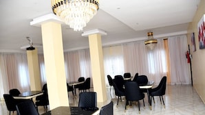 A spacious dining area with black tables and chairs, a chandelier, and large windows with curtains. - Joyrich Hotel (Epe)