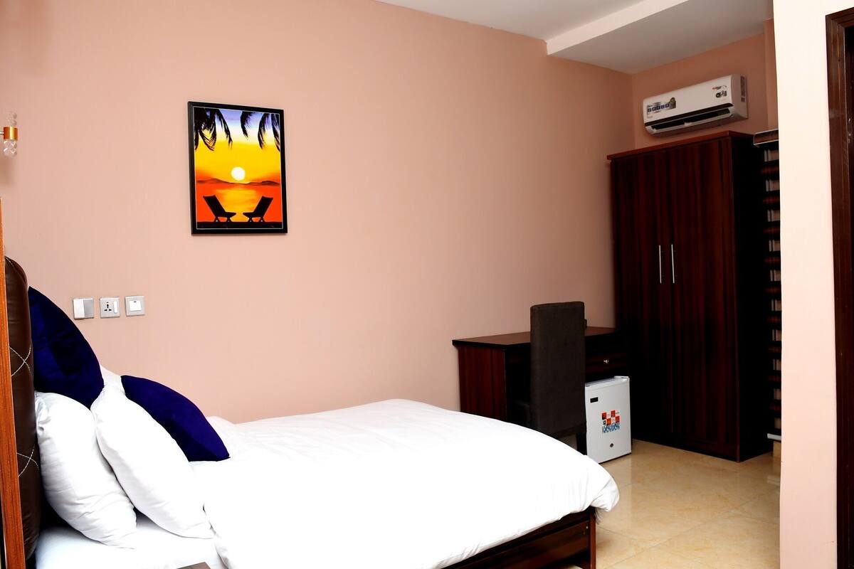 A bedroom with a bed, a wall-mounted air conditioner, a small desk, and a wardrobe.