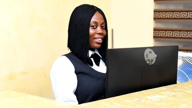 A person sitting at a table with a laptop, wearing a vest and a bow tie. - Joyrich Hotel (Epe)