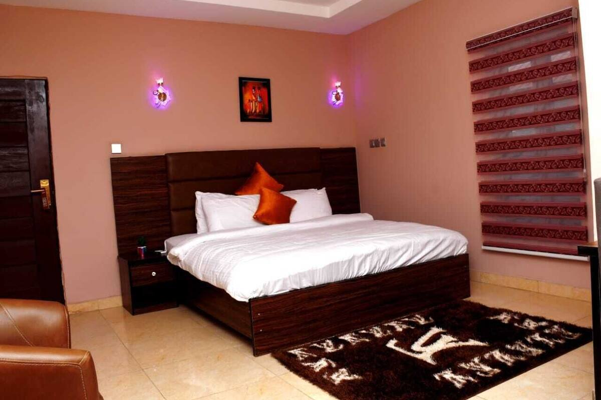 A bedroom with a large bed, a nightstand, a brown leather chair, and a patterned rug.