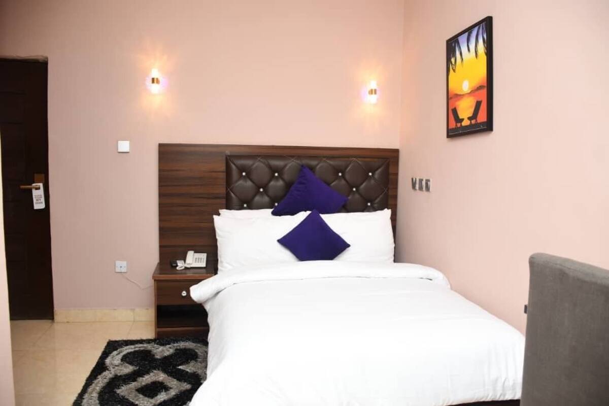 A neatly made bed with a tufted headboard, a bedside table with a phone, and a wall-mounted painting.