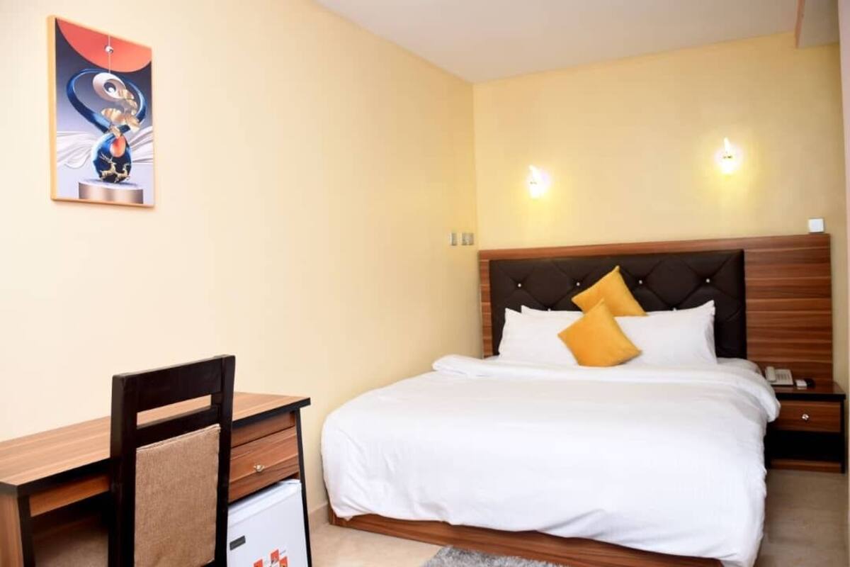 A hotel room with a bed, bedside table, chair, and a painting on the wall.