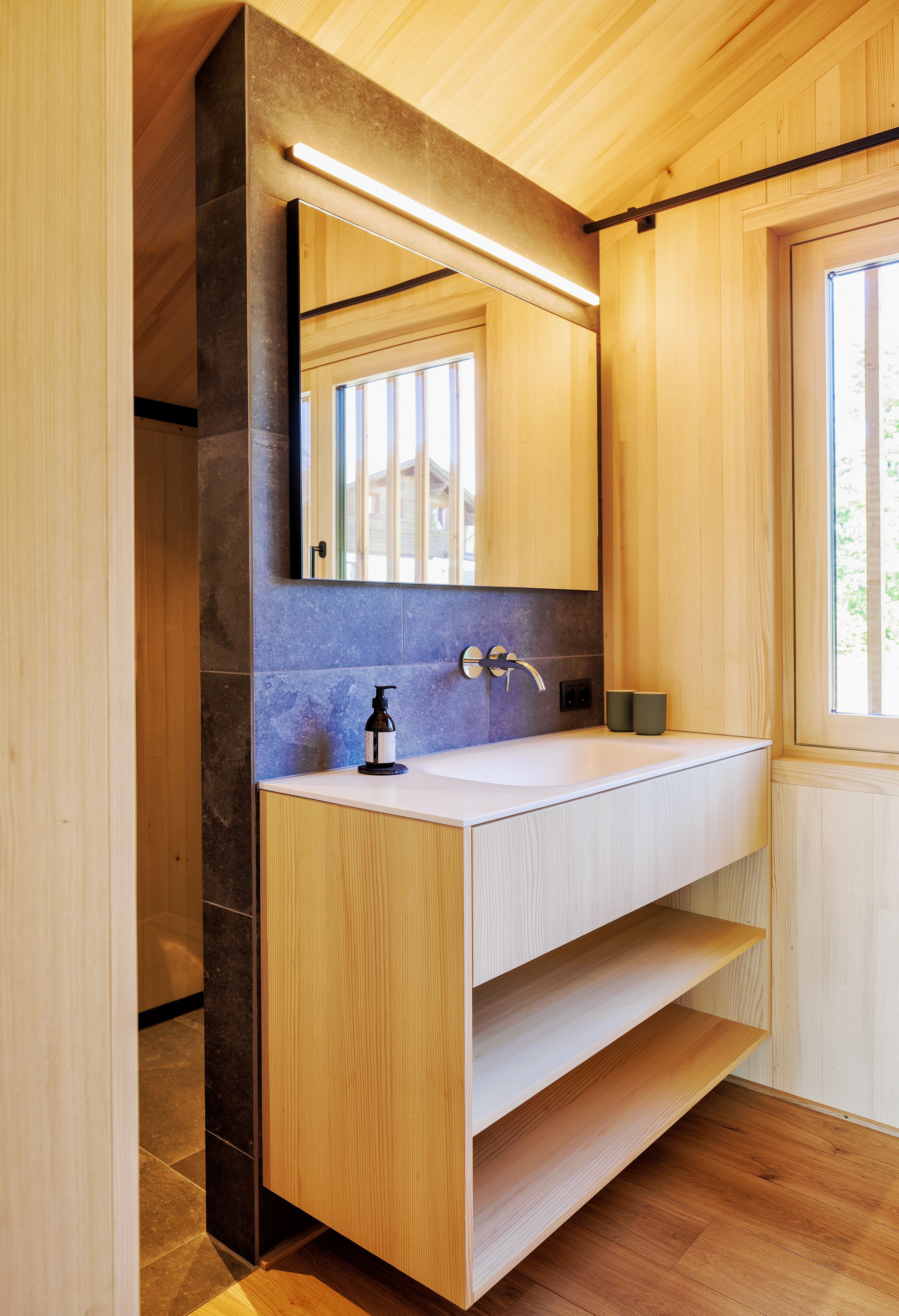A modern bathroom with a wooden vanity, a large mirror, and a built-in shelf.