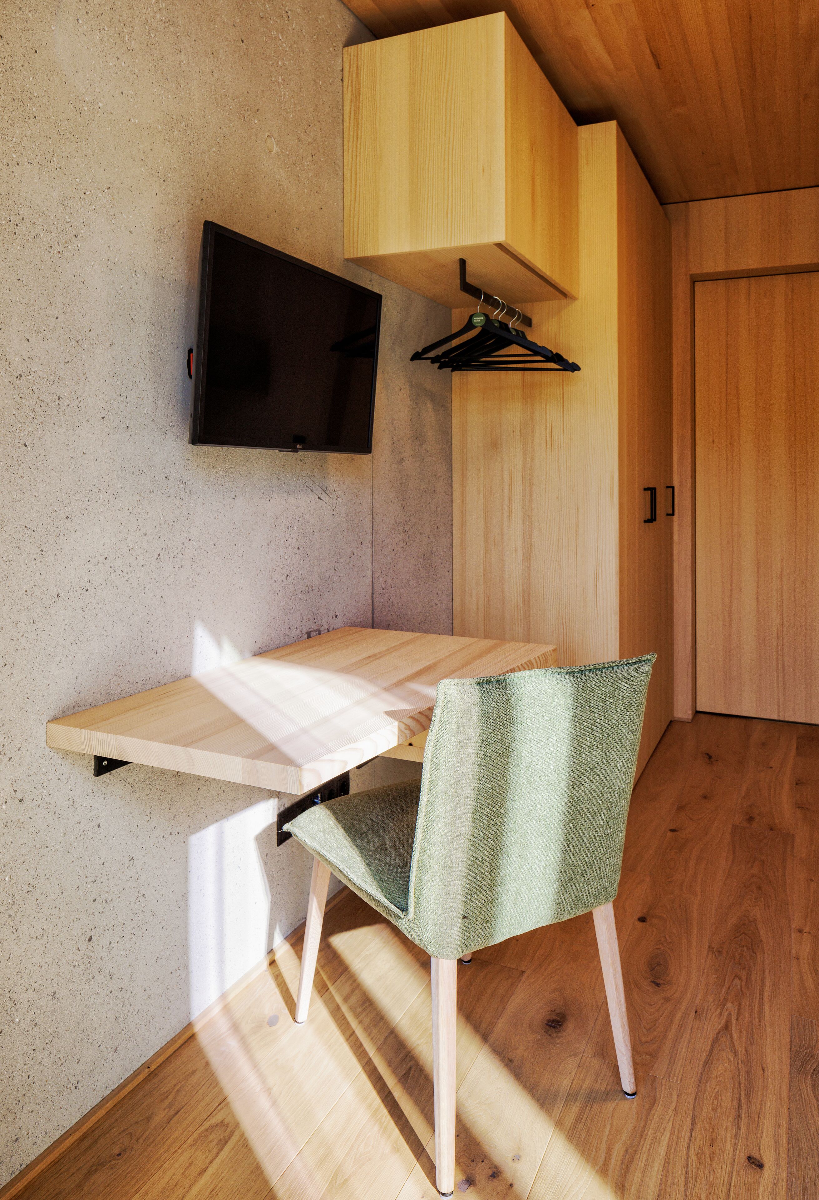 Un bureau en bois, un téléviseur fixé au mur, une chaise et un meuble en bois.