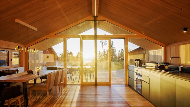 A modern kitchen with a wooden ceiling, a dining area with chairs and a table, and a large sliding glass door leading to an outdoor deck. - Pfänder Glück (Lochau)