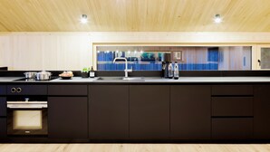 A modern kitchen with a wooden ceiling, built-in appliances, and a large window offering a view of the outdoors. - Pfänder Glück (Lochau)